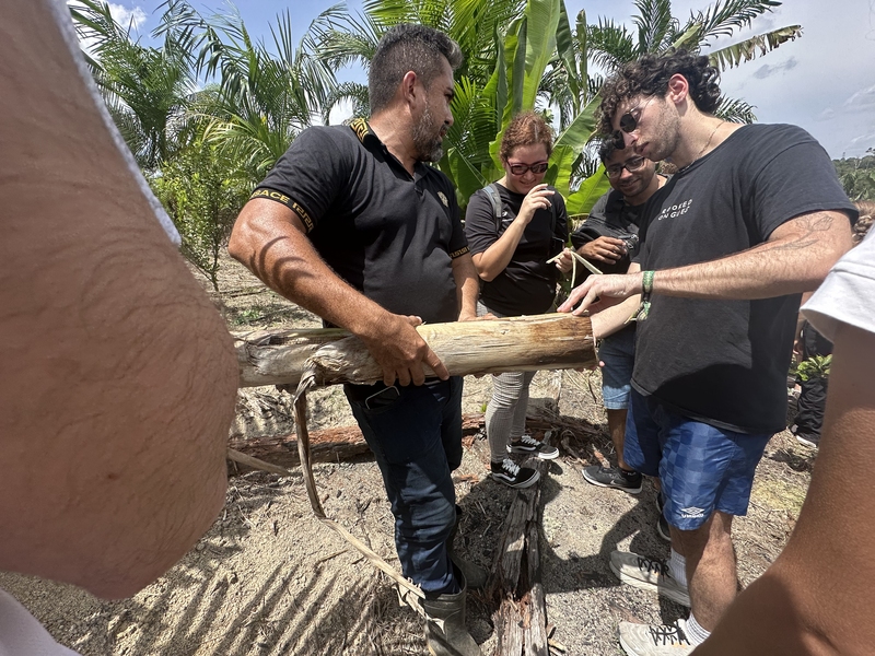 two men hold a piece of wood and two other people watch while standing outside