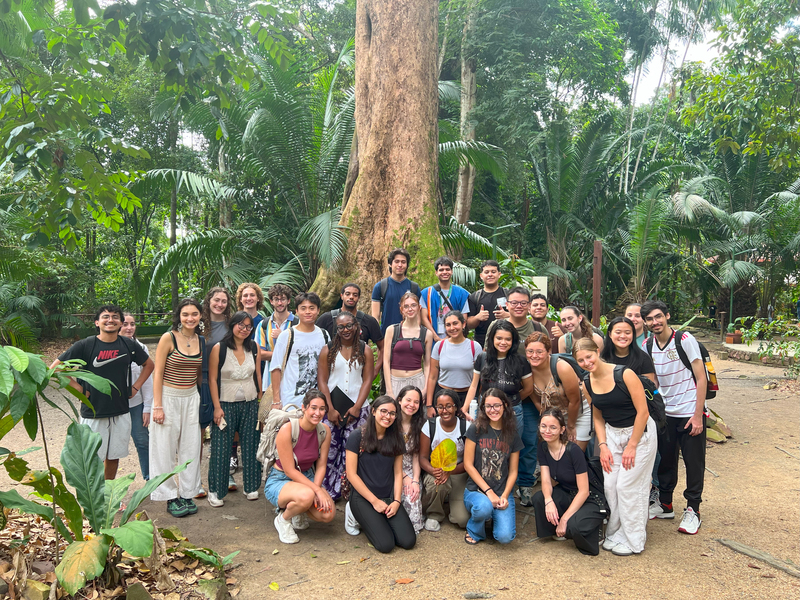 Group of more than two dozen students pose under a tree in a wooded area
