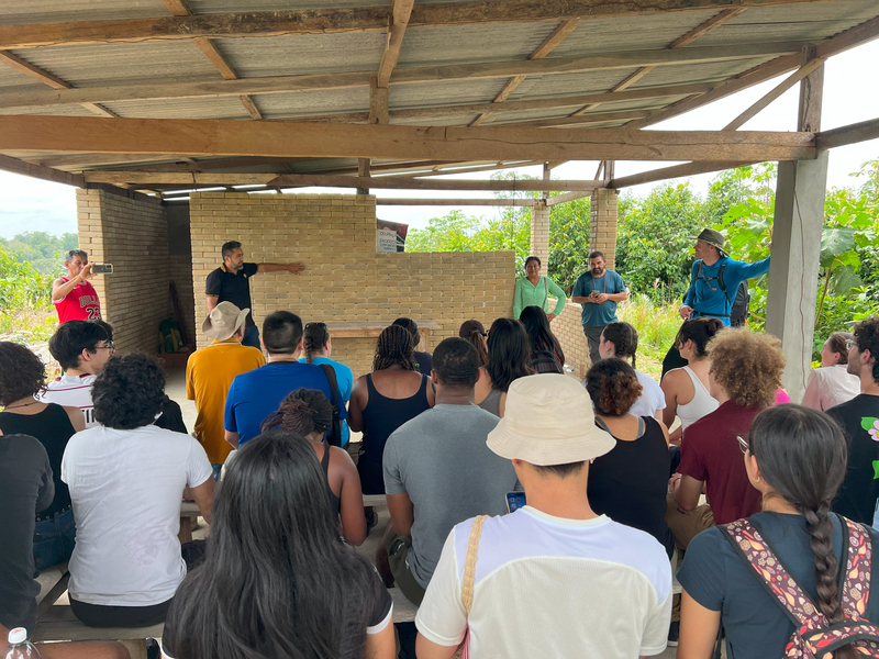 a man stands in front of a brick wall under an open structure, while a crowd looks on