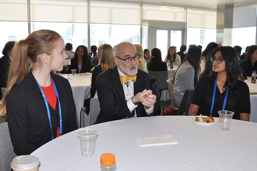 Matthew Frosch talks with two students seated at a round table bearing food and beverages