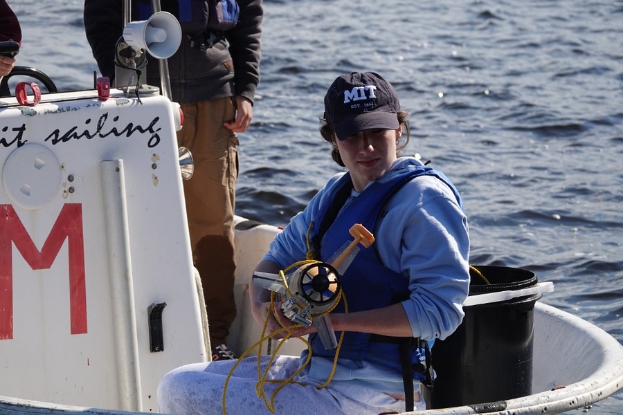 An MIT student on a boat in the Charles River holds an autonomous underwater vehicle
