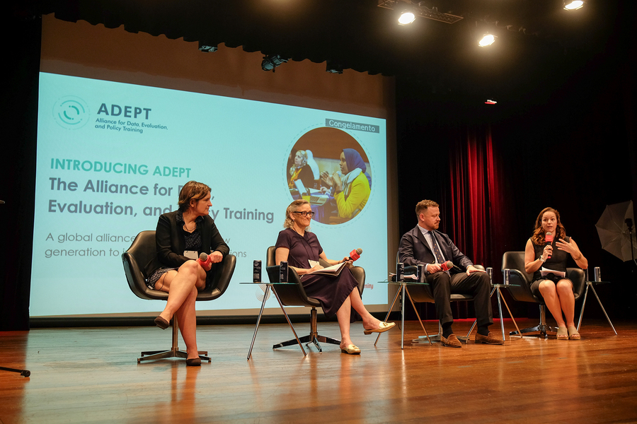 Esther Duflo, Sara Fisher Ellison, George Richards, and Sarah Kopper are seated on a stage, with an image projected behind them with the words "Introducing ADEPT, Alliance for Data, Evaluation, and Policy Training."