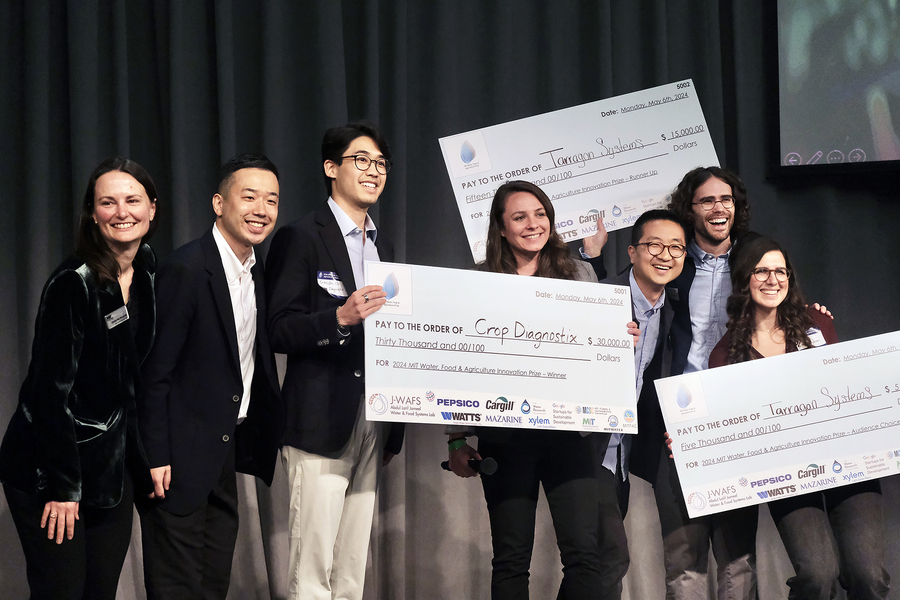 Seven individuals smiling on a stage while holding three large checks