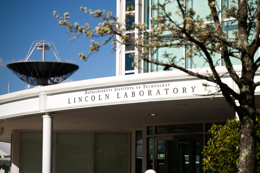The exterior main entrance of Lincoln Laboratory, with a radar antenna pointed skyward in the background.