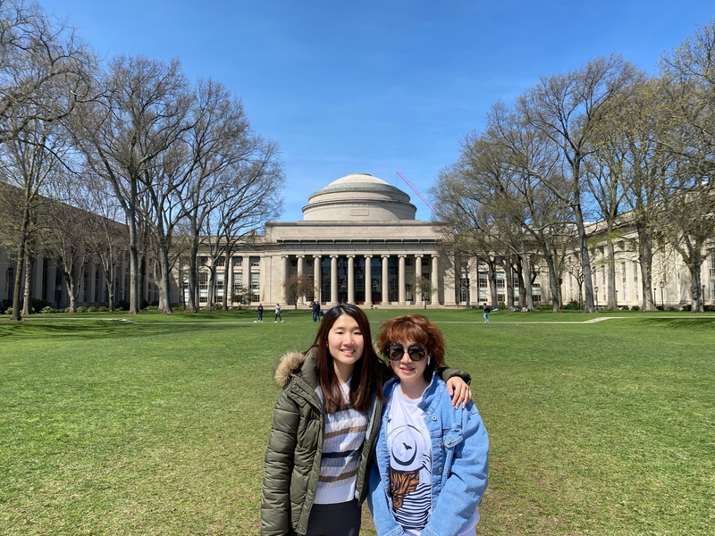 Liang hugs her mom in front of MIT's iconic Great Dome on a clear, sunny day.