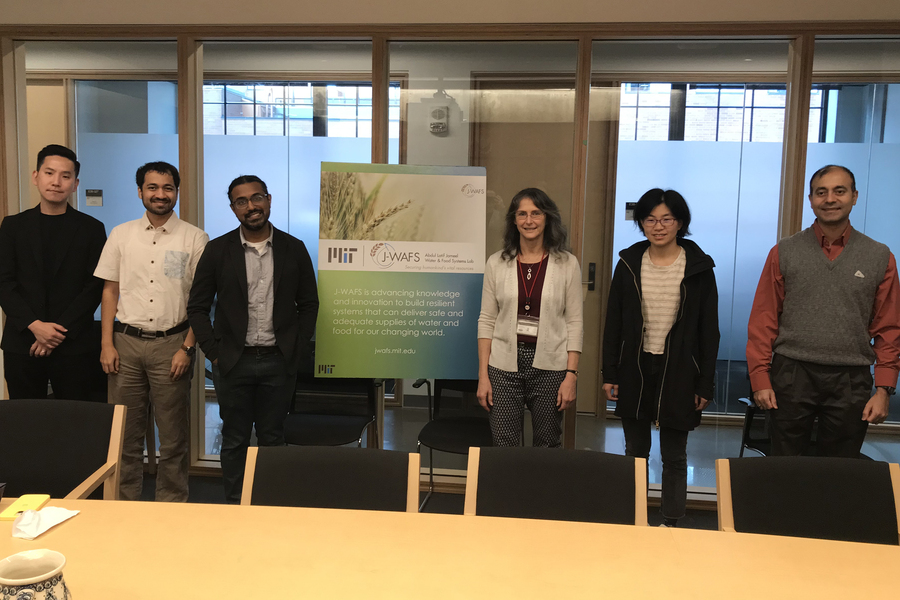 A group of six people standing in a conference room, posing for a photo beside a J-WAFS sign