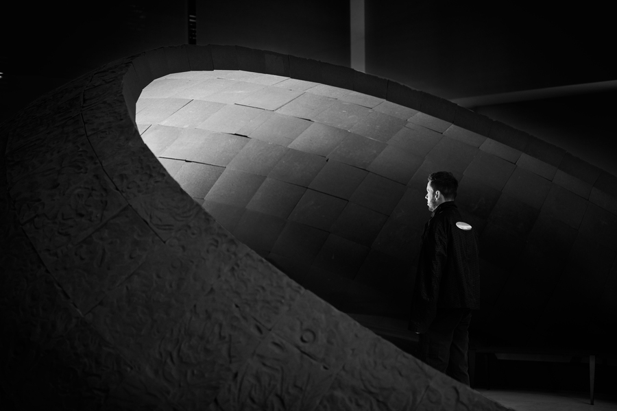 A person stands in a dimly lit space, facing a large, curved, sculptural structure.