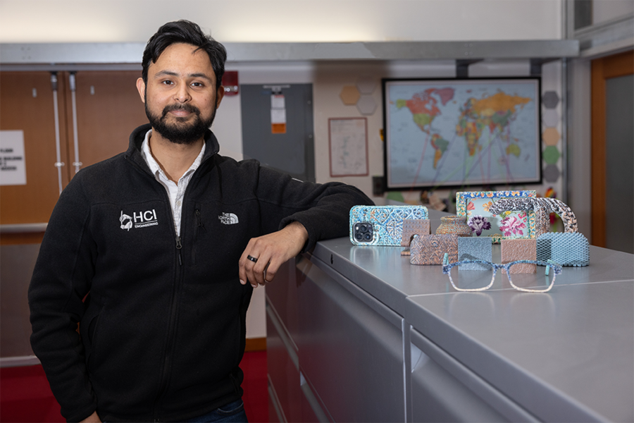 Faraz Faruqi stands next to colorful and texturized objects created by TactStyle, including eyeglass frames, a phone case, a pot, and picture frame.