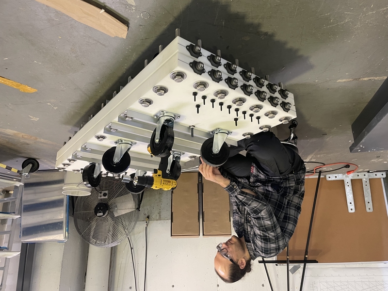 A man with a power drill squats to assemble a rectangular, industrial-scale desalination system with wheels