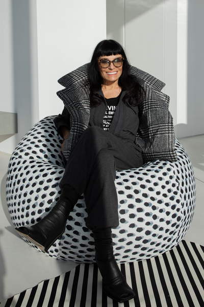Norma Kamali, dressed in black, sits with crossed legs on a black-and-white polka-dot beanbag chair