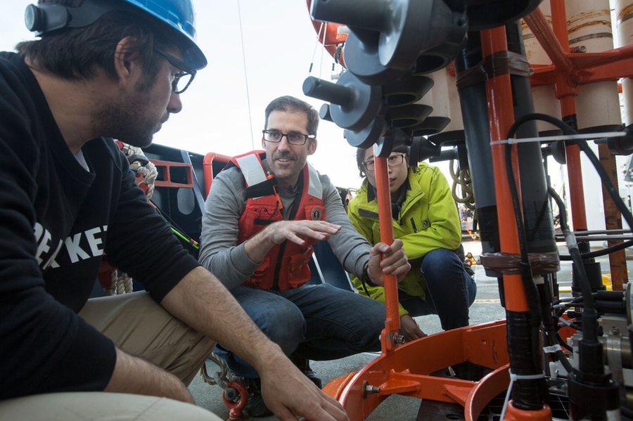 Three researchers crouch, gathered around equipment used to take measurements of ocean water columns