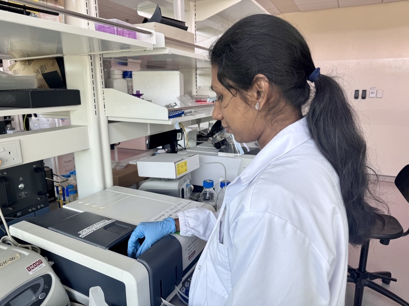 Woman in a lab coat inserting a sample into a machine about the size of a printer.