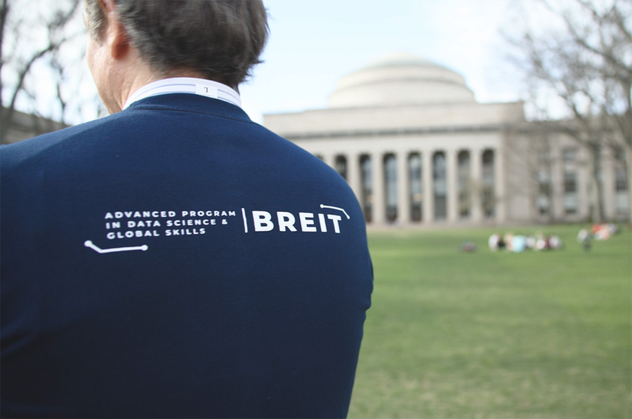 Ivo Saona stands on the MIT Killian Court with his back to the camera. His jacket says "BREIT Advanced Program in Data Science and Global Skills."