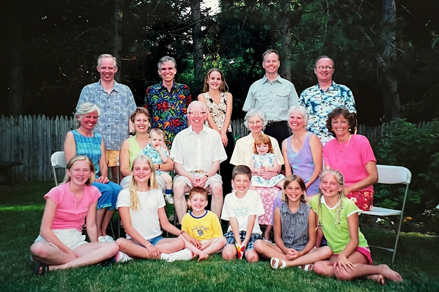 19 people pose for a family portrait on a lawn in front of trees