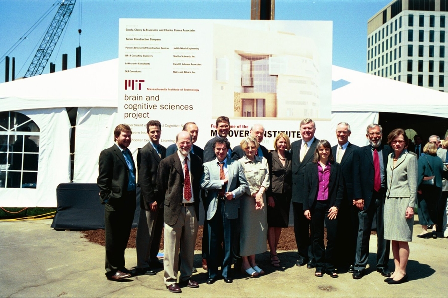 A group of 15 men and women in business attire pose in front of a construction sign