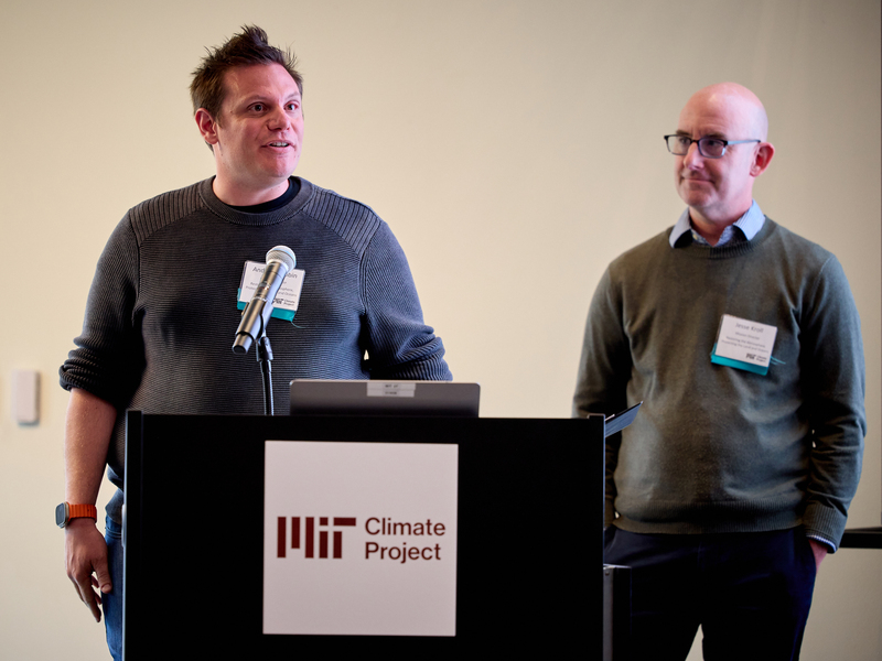 Andrew Babbin stands behind a lectern. To his left stands Jesse Kroll.