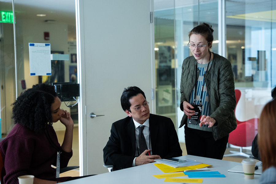 Caitlin Morris, standing in a small room, talks with two people seated at a conference table