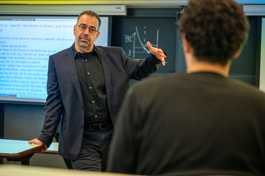 Daron Acemoglu, leaning on a desk, teaching class