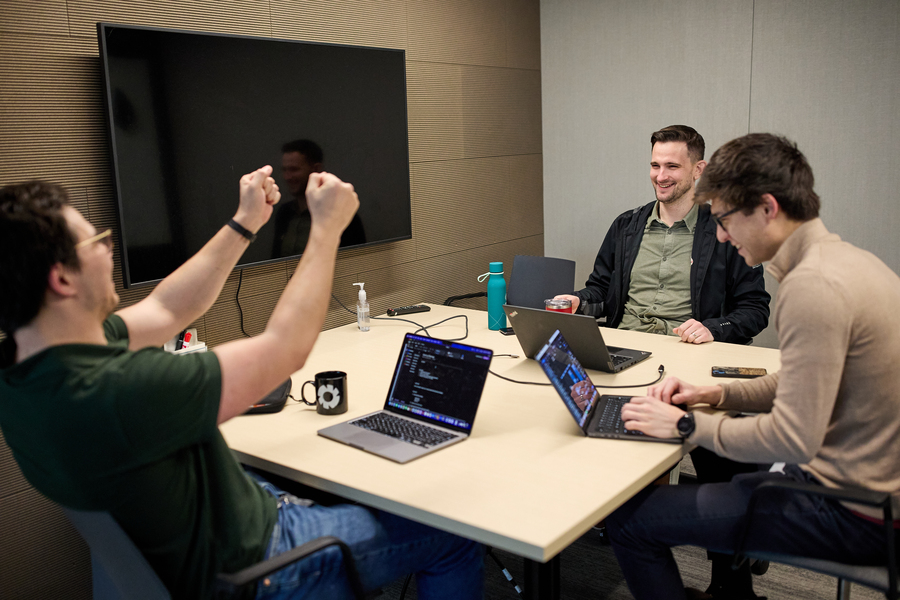 Dave Brown sits at a small table with two other men. All of them have open laptops in front of them and a beverage.