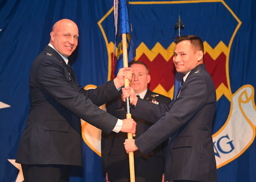 Brian Brooks and Erik Lin-Greenberg grip a ceremonial flag pole while Cary Mueller looks on.