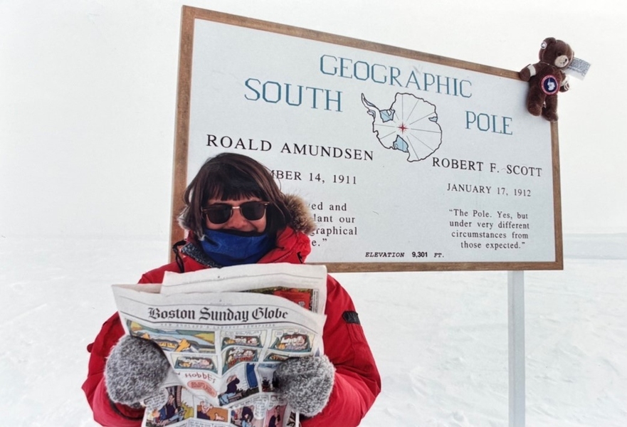 Usha Lee McFarling, dressed in winter clothing, stands at the South Pole Station in Antarctica, holding up a Boston Sunday Globe comics section. 