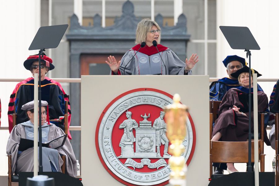 Sally Kornbluth, in ceremonial Commencement garb, speaks at a large podium featuring the MIT seal