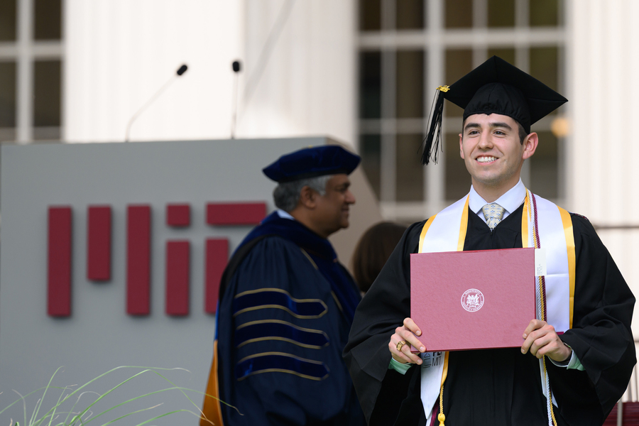 Smiling graduate wearing cap and gown holds up his diploma.