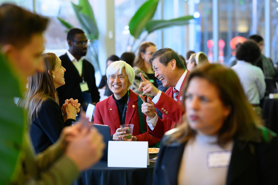 Three people laugh during a conversation in a crowded room.