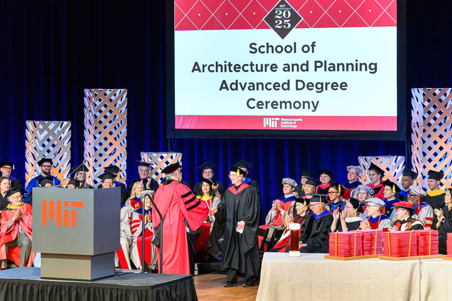 MIT faculty in graduation robes sit on a stage with a display that says "School of Architecture and Planning Advanced Degree Ceremony"