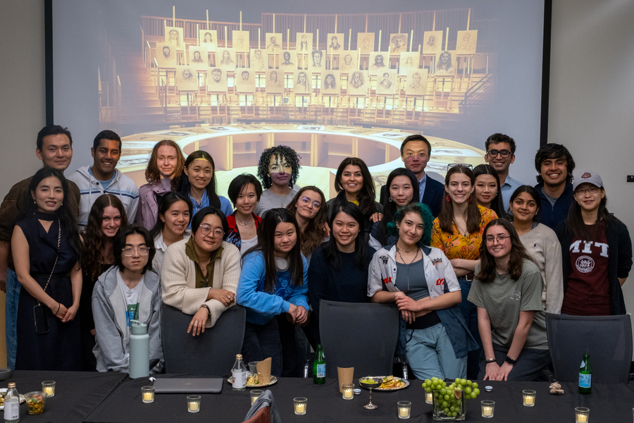 About 25 students pose behind a table and in front of a screen with Es Devlin