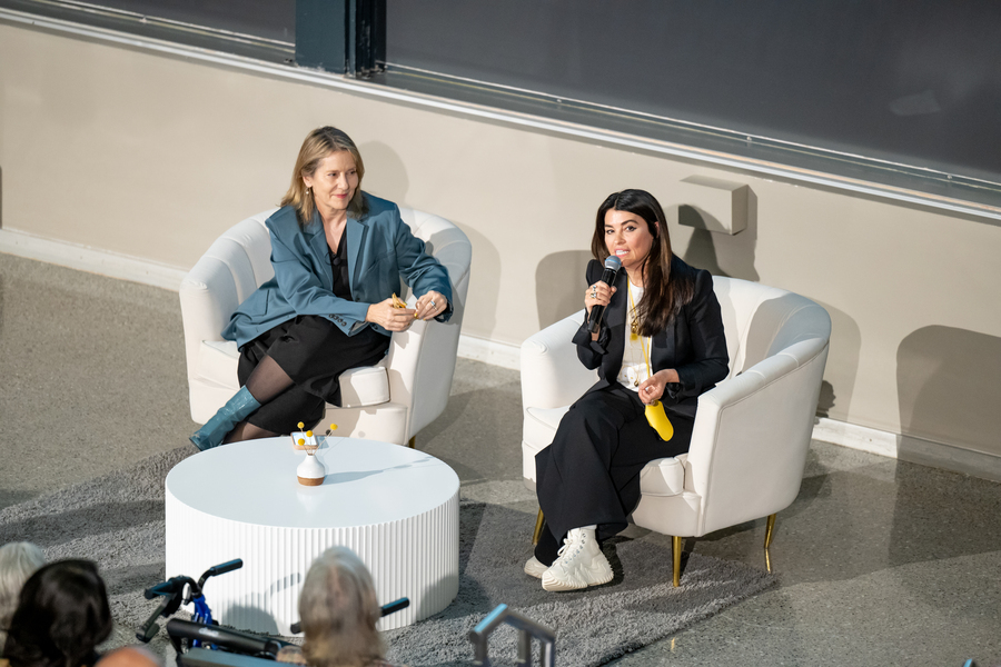 Paola Antonelli and Es Devlin sit on white chairs facing an audience; one speaks into a microphone