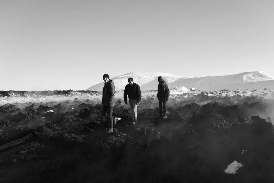 Grayscale photo of three people walking on a barren lava field
