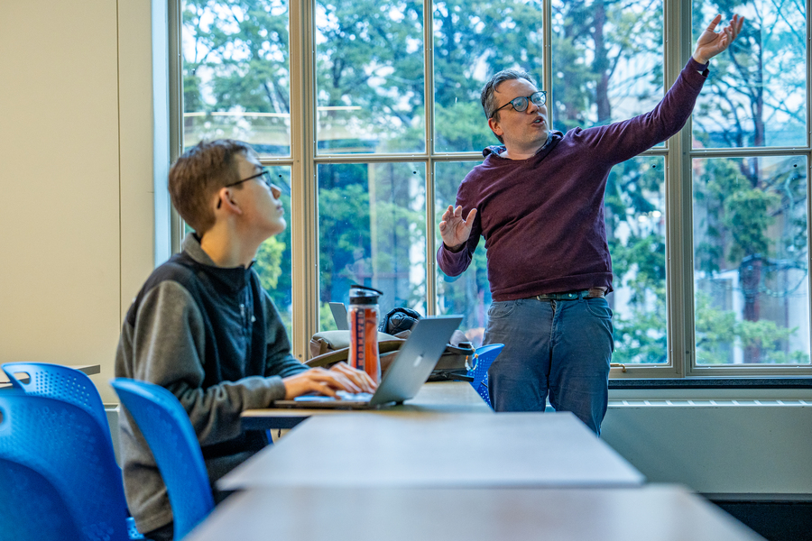 Daniel Hidalgo, standing in front of a classroom window, gestures while speaking to students.