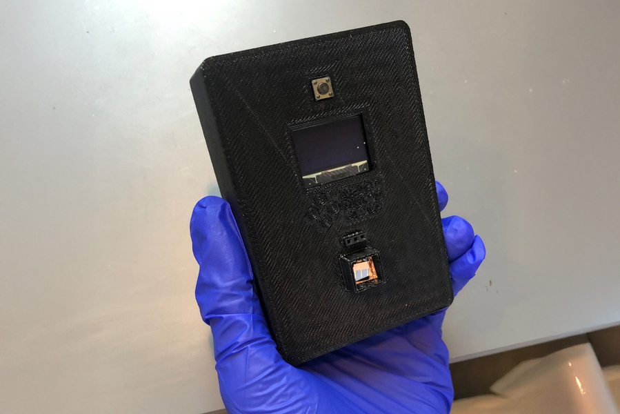 A black rectangular sensor held by a gloved lab technician.