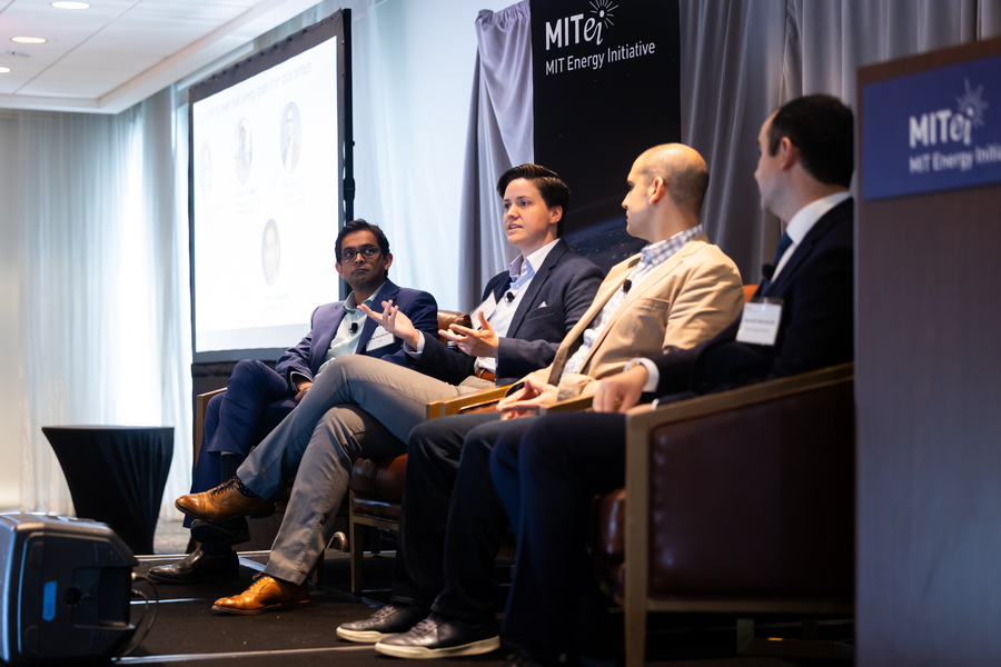 Panelists sit in chairs in a row on a stage.