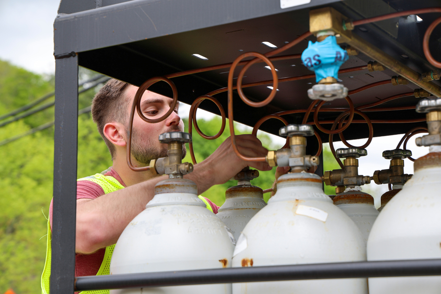 A man adjusts tubing in a rack of large compressed gas tanks.
