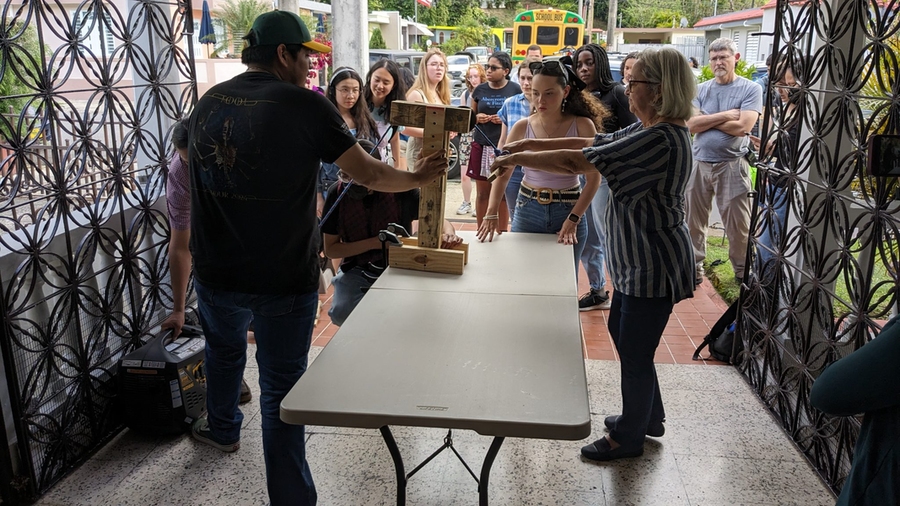 While at least a dozen people look on, a senior citizen tests a pulley device to help her start a gasoline-powered electric generator