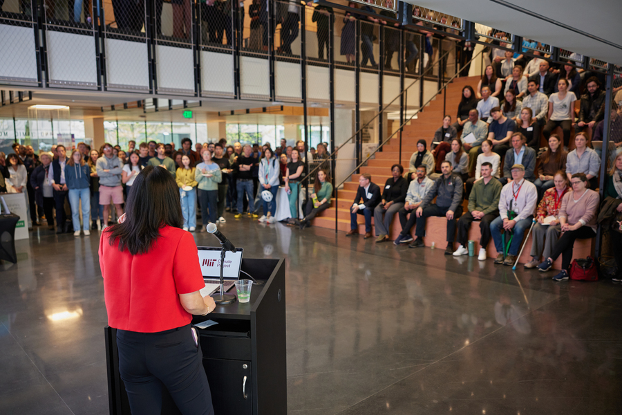 Evelyn Wang, with her back to the camera, addresses around 100 people who are either standing or sitting in a lecture space with tiered seats