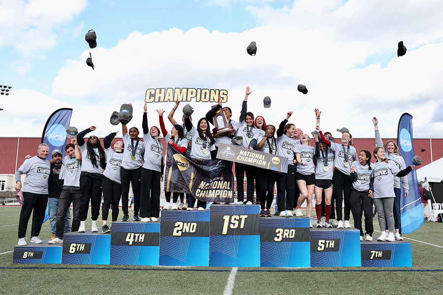 About 20 MIT women's team members and three coaches celebrate on the podium by throwing their hats in the air 