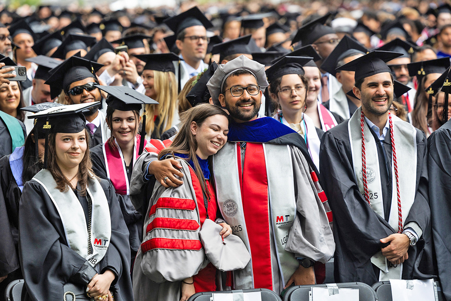 In the front row of a large audience of new MIT graduates wearing caps and gowns, Erin Tevonian and Viraat Goel smile in a side hug.