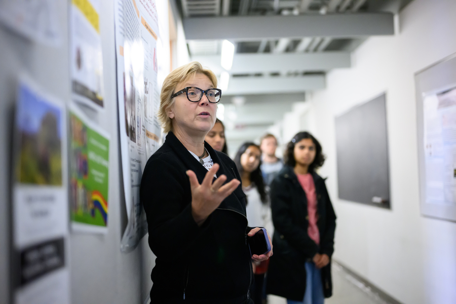Linda Griffith stands next to scientific poster in hallway and speaks to students