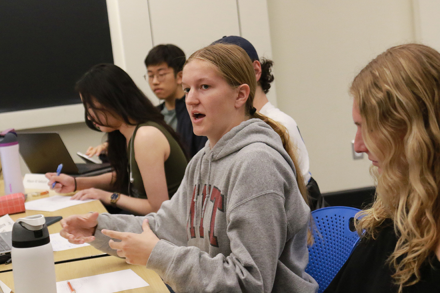 Five students sitting at a classroom table, one of whom is almost entirely obscured.