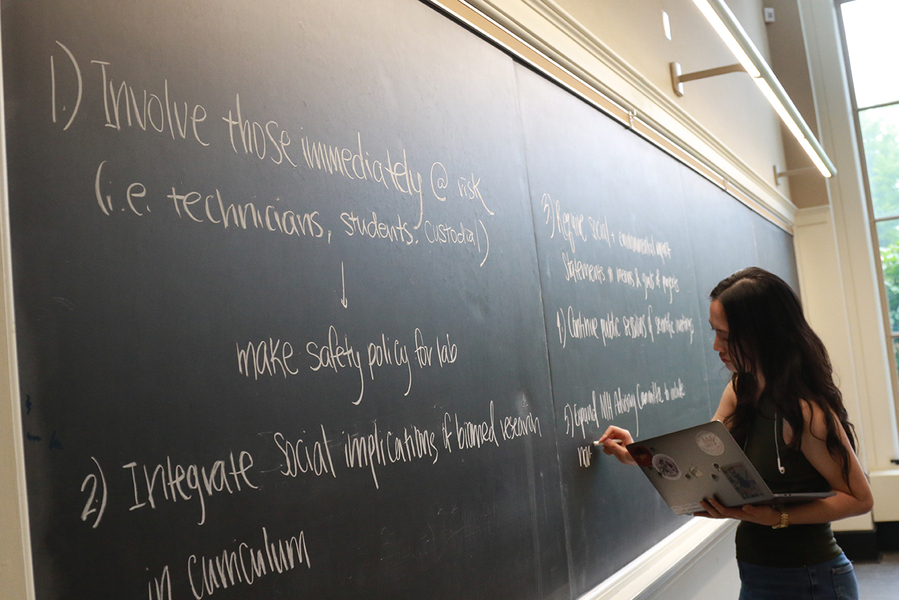 Seen in profile, Jessie Lin holds a laptop in one hand while writing on a chalkboard.