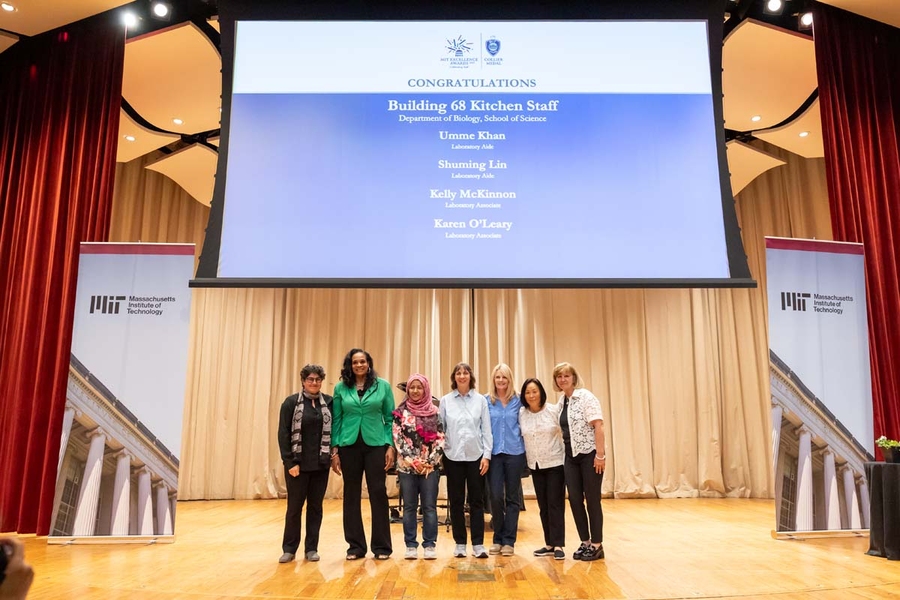A group of seven people stand on a stage together.