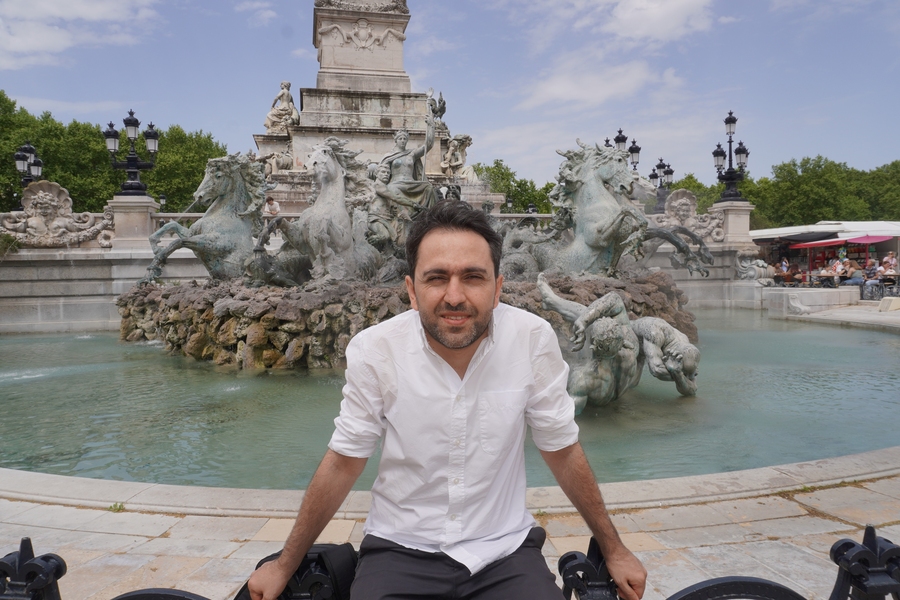 Gevorg Minasyan sits on the edge of classical sculpture fountain on a partly cloudy day.