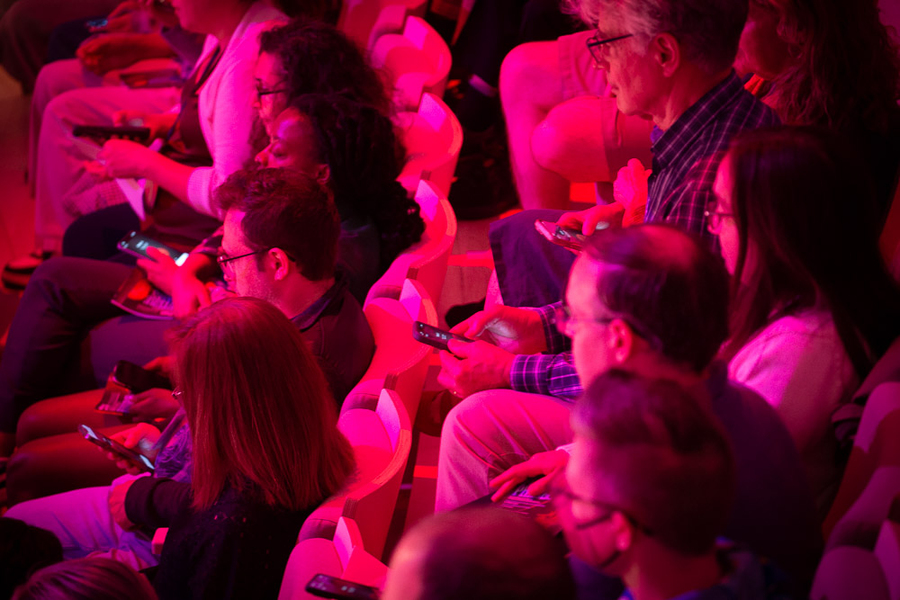 Closeup on about 10 red-lit audience members, all holding cellphones