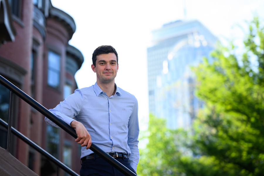 Vincent Rollet standing outside in Boston. An out-of-focus brownstone is visible to the left, with the hazy Prudential Center behind him.