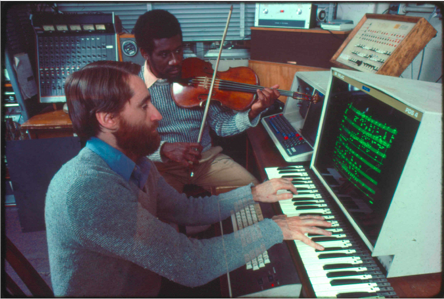 A young Barry Vercoe seated at keybord and computer monitor while Marcus Thompson, seated behind him, accompanies on violin
