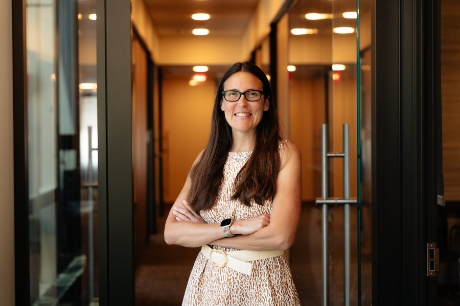 Caroline Uhler stands in front of two open glass doors leading to a hallway.