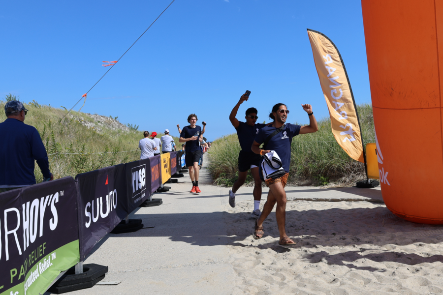 People in athletic wear joyfully cross a sandy race finish line, hands raised in victory.